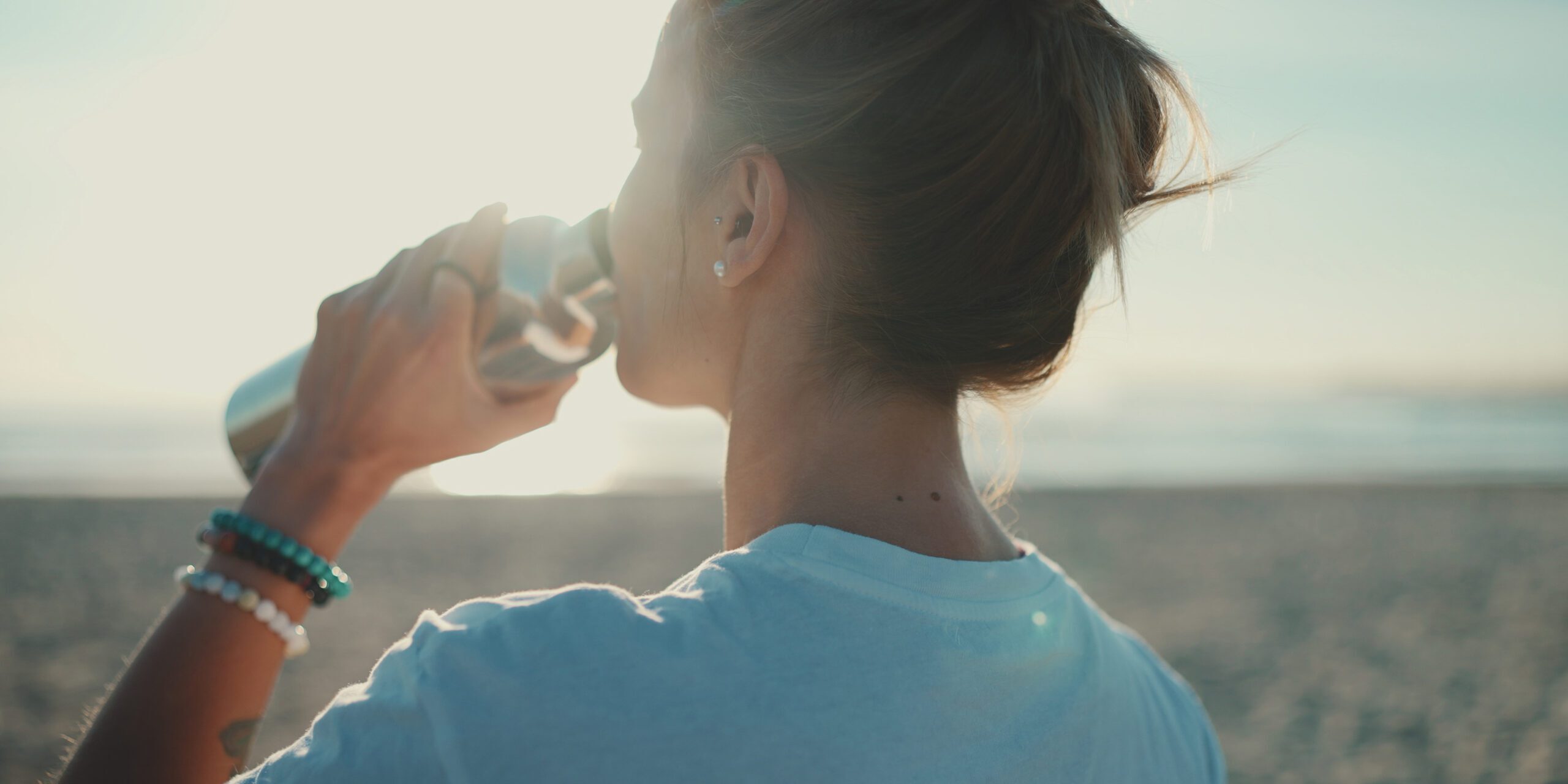 Back view of woman drinking water after yoga practice on the bea