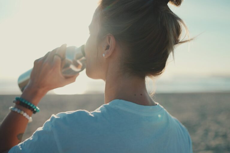 Back view of woman drinking water after yoga practice on the bea